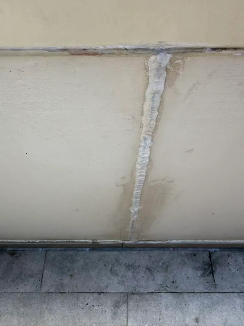 A vertical sealant line crosses a horizontal junction in the painted wall panels.