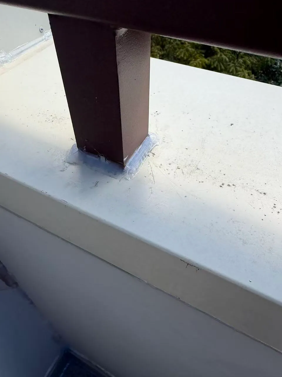 Sealant surrounds the base of a brown railing post on the balcony capping.