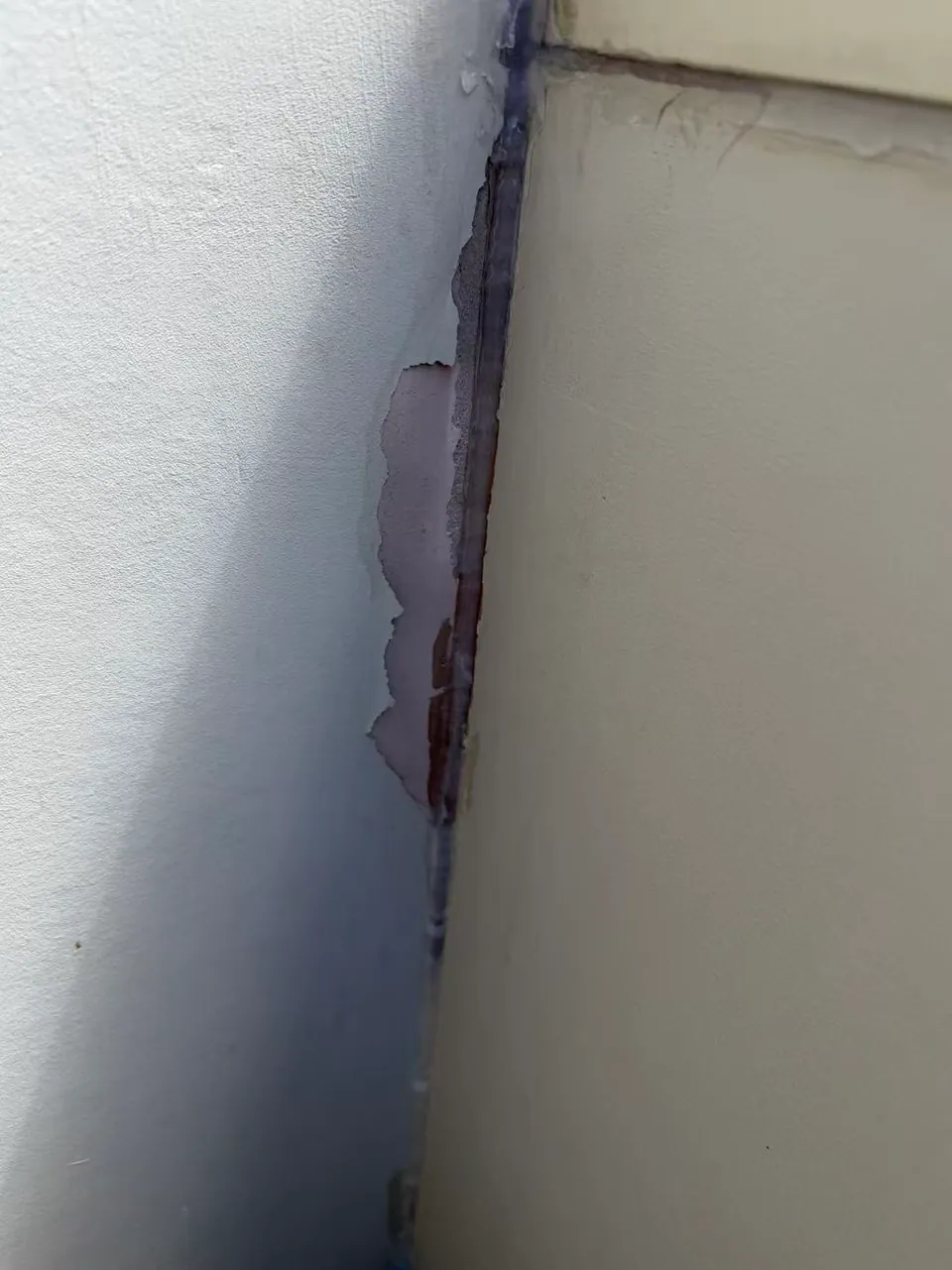 Peeling paint and an exposed edge are visible beside the vertical wall junction.
